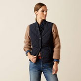 Woman wearing a navy quilted gilet over a brown sweater on a beige background